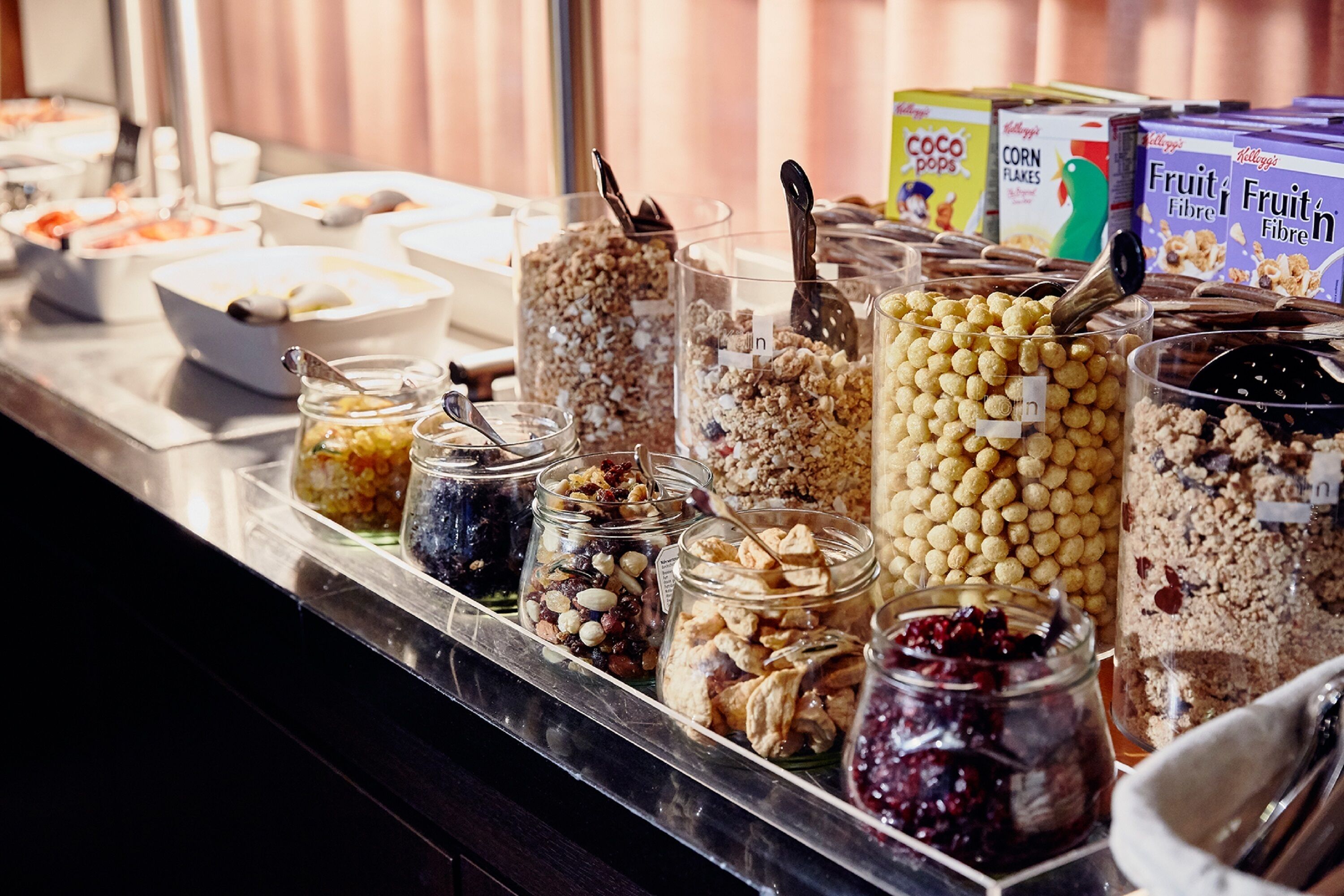 Een buffet met diverse etenswaren en bakken, waaronder ontbijtgranen, noten en fruit.