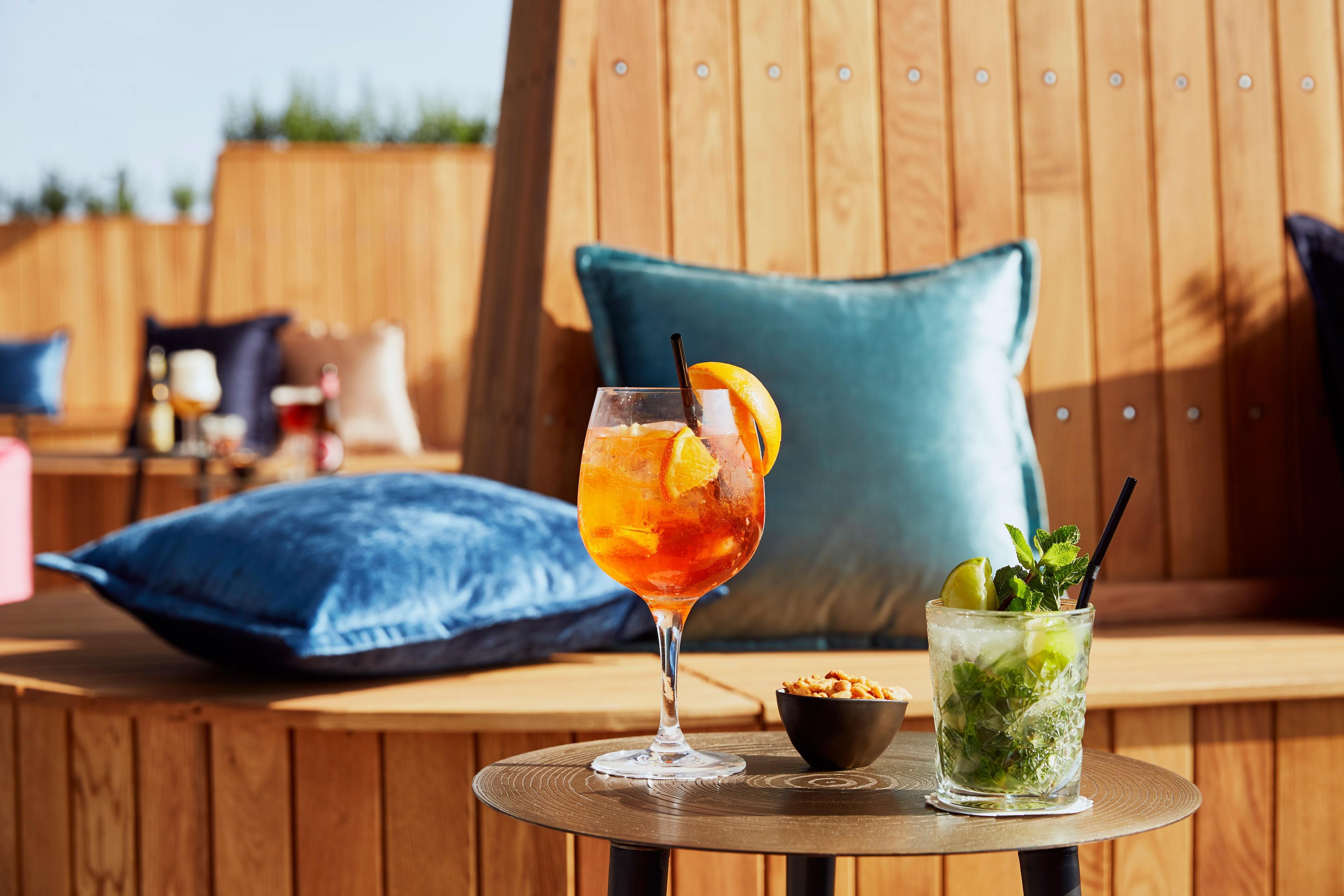 A glass of iced drink with a slice of orange and mint garnish on a round table.