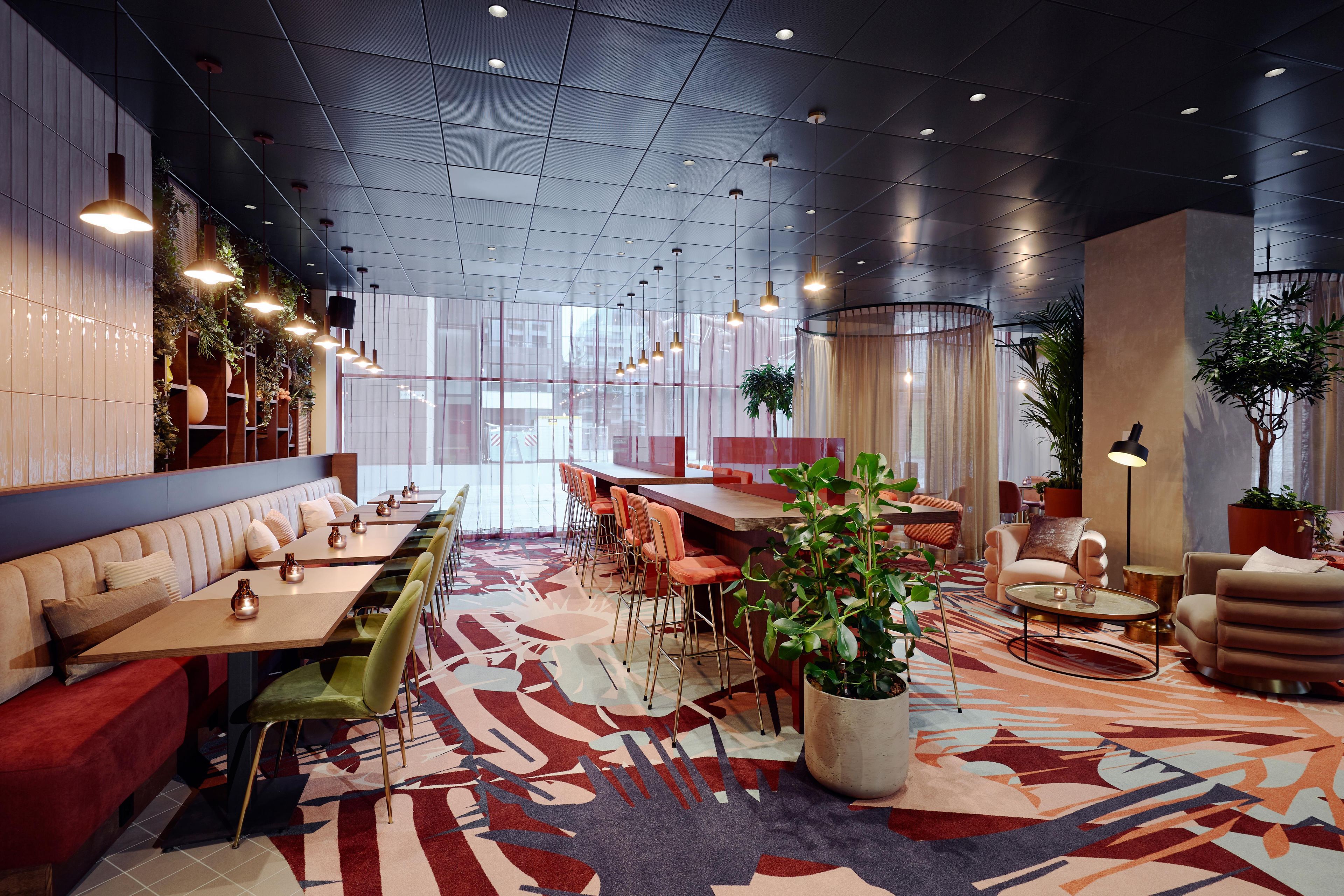 Un intérieur de restaurant moderne, caractérisé par de hauts plafonds, des luminaires suspendus et un tapis à motifs.