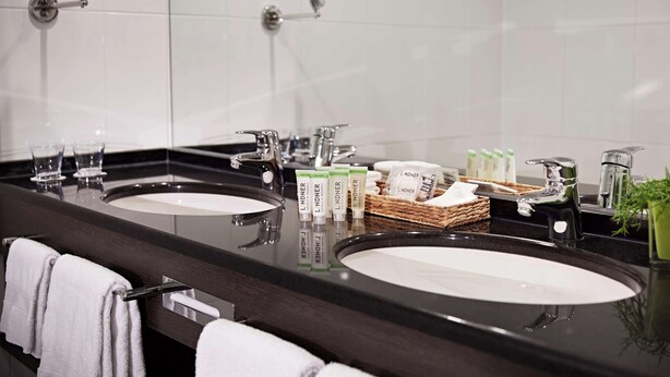 A modern bathroom with two sinks, a mirror, and toiletries. - Lindner Hotel Antwerp, part of JdV by Hyatt (Antwerp)