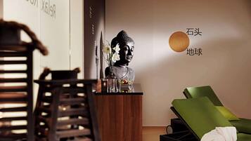 Ein Zimmer mit Buddha-Statue, einem grünen Lounge-Sessel und einem Holztisch mit Blumen in einer Vase.