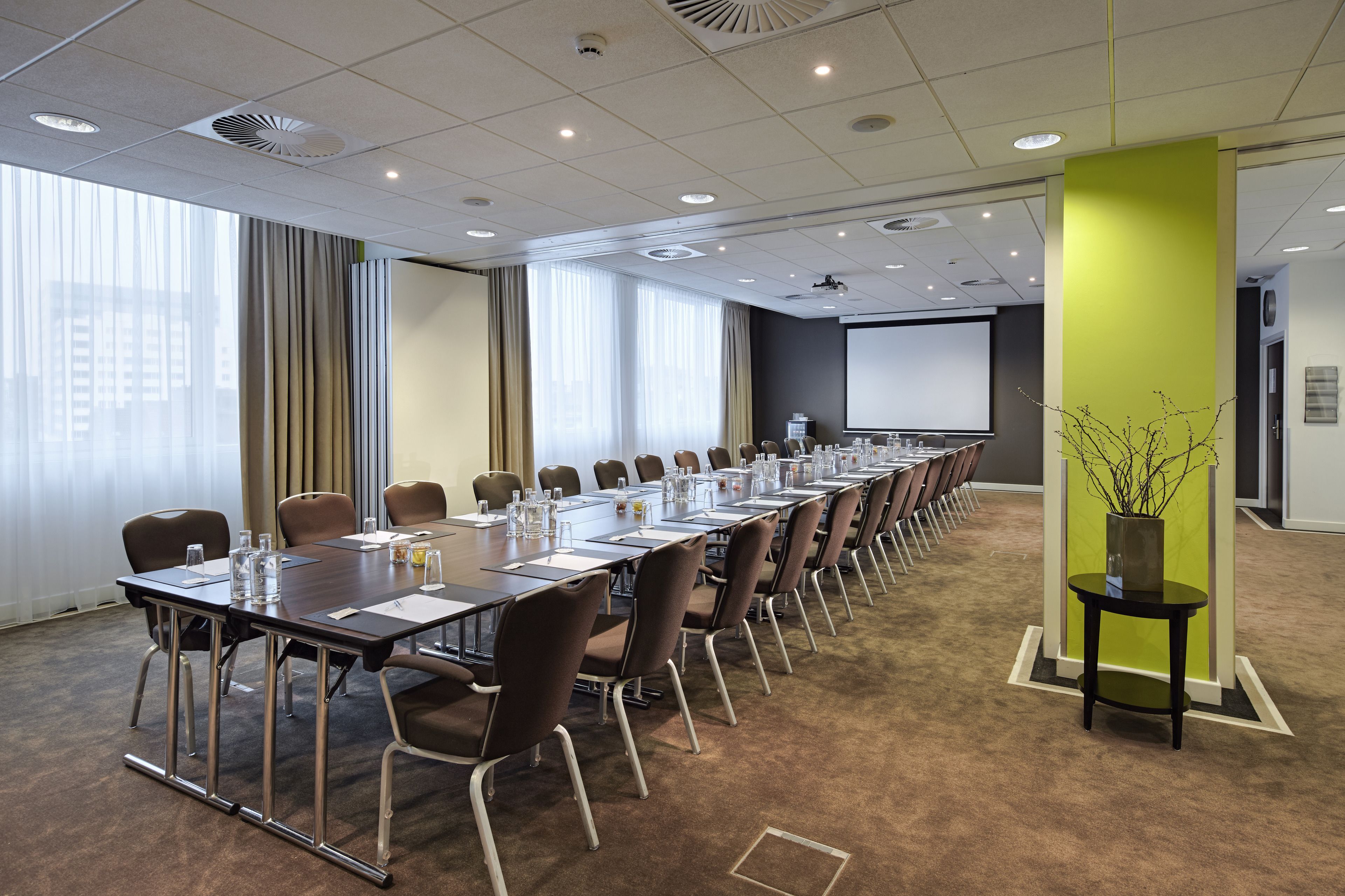A conference room with a long table, chairs, and a projector screen.