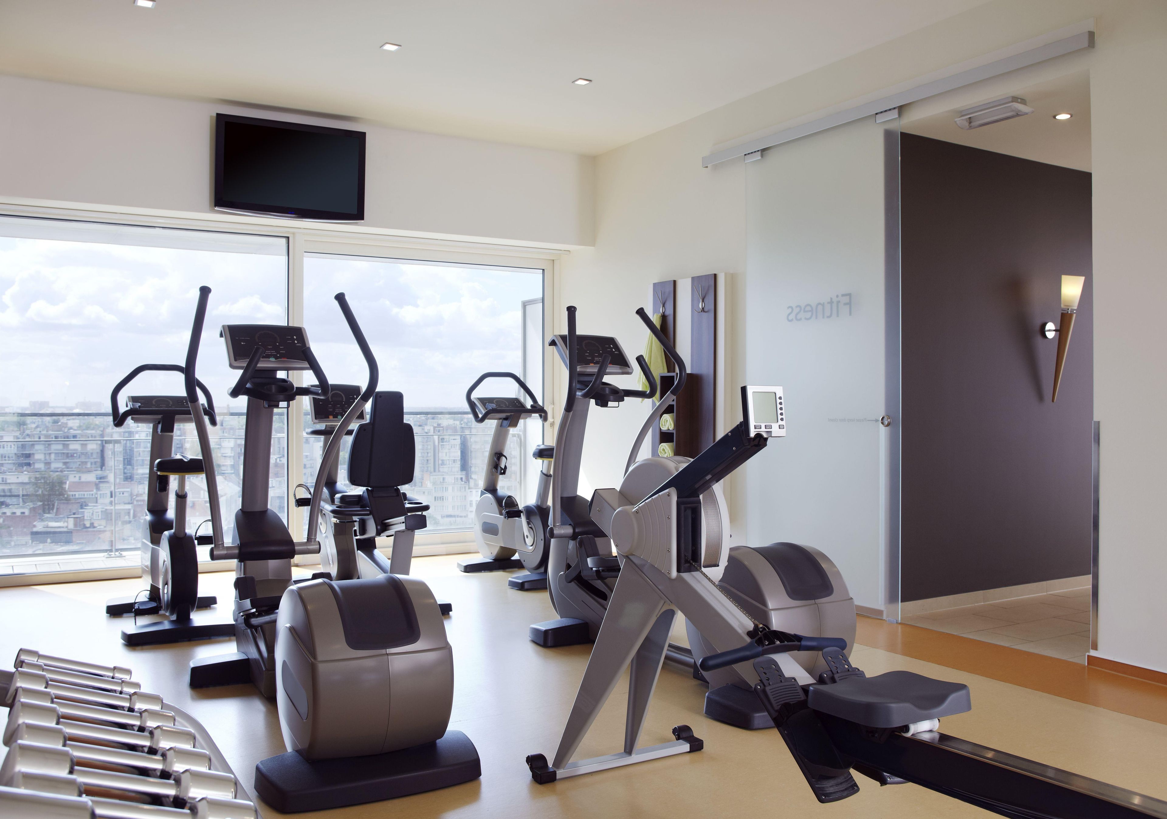 A modern gym with various cardio machines, large windows, and a city view.