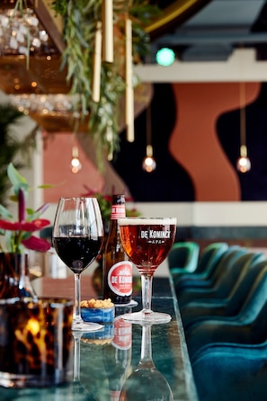 A bar area with two glasses of wine, a bottle of De Koninck beer, and a bowl of nuts on the counter.
