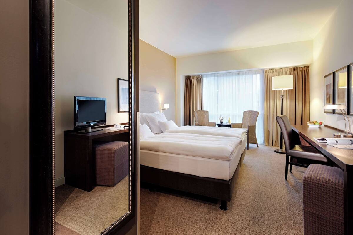A hotel room with a large bed, a desk with a computer, a chair, and a television.