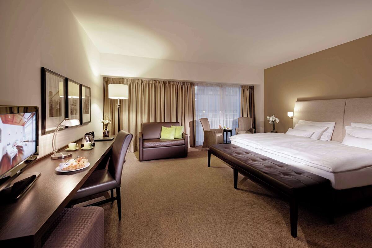 A hotel room with a large bed, a desk with a chair, a sofa, and a television.