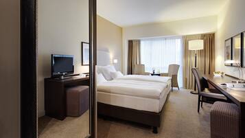 Une chambre d’hôtel équipée d’un lit, d’un bureau, d’une chaise, d’une télévision et d’un grand miroir.