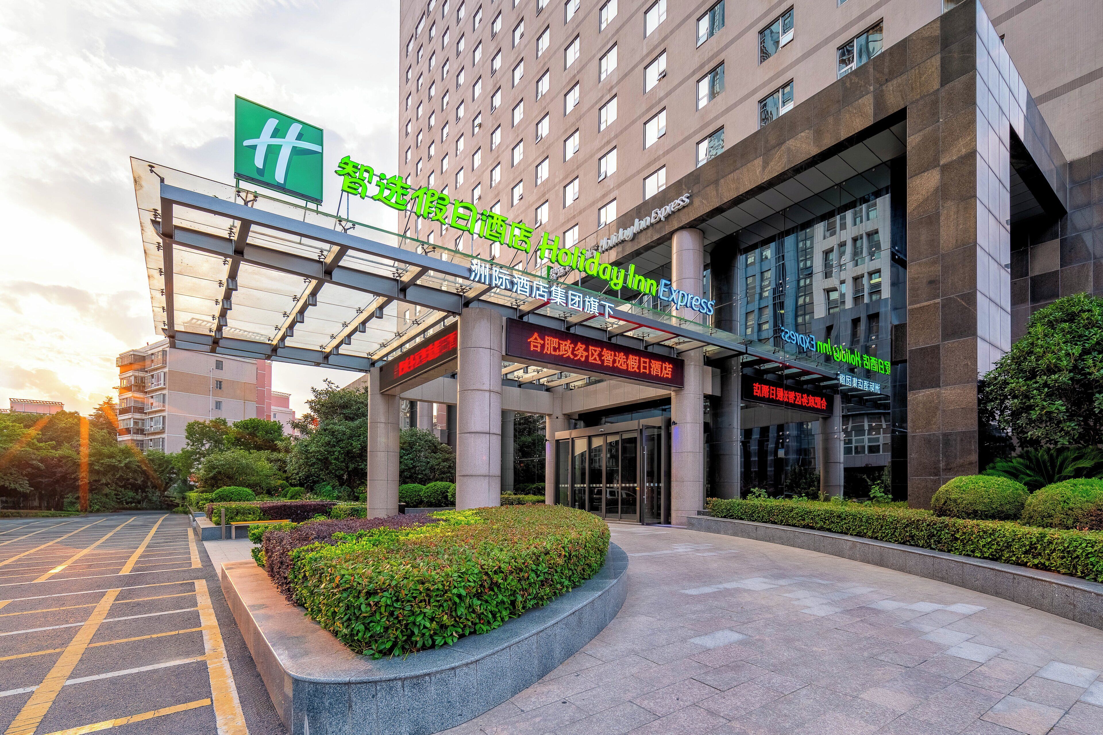 A hotel entrance with a modern design, a covered walkway, and a landscaped area with hedges.