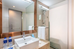 A modern bathroom with a white sink, two bottles of water, a mirror, and a glass shower enclosure.
