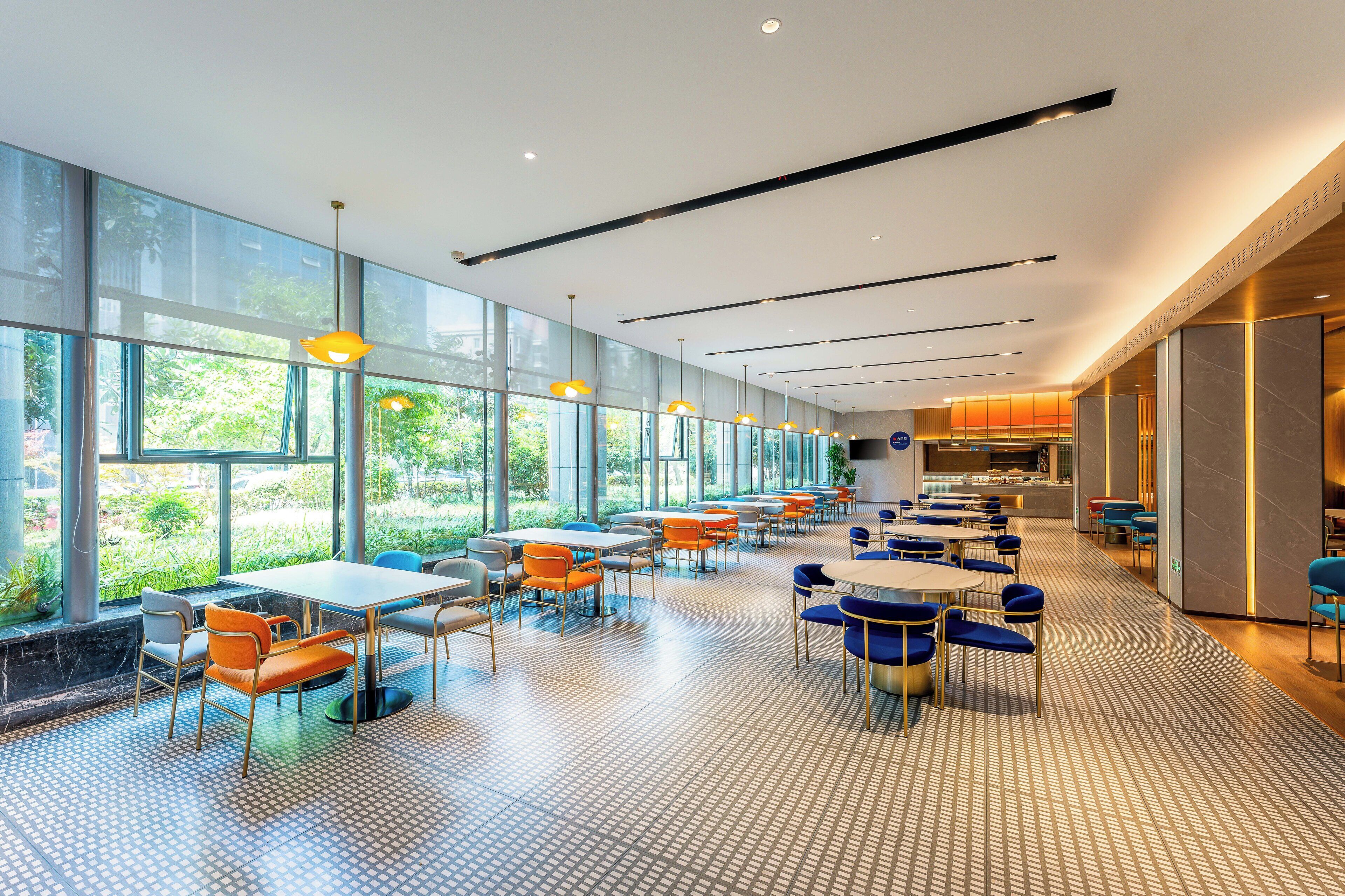 A spacious indoor area with large windows, tables, and chairs arranged for dining.