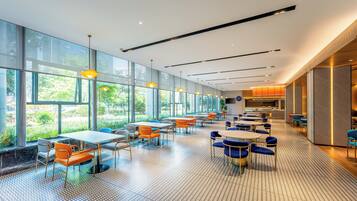 A spacious indoor area with large windows, tables, and chairs arranged for dining.