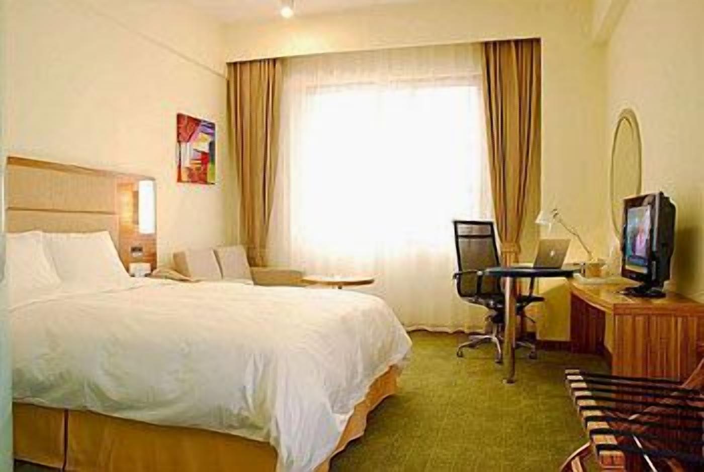 Une chambre d’hôtel avec un grand lit, un bureau avec un ordinateur, une télévision et une chaise.