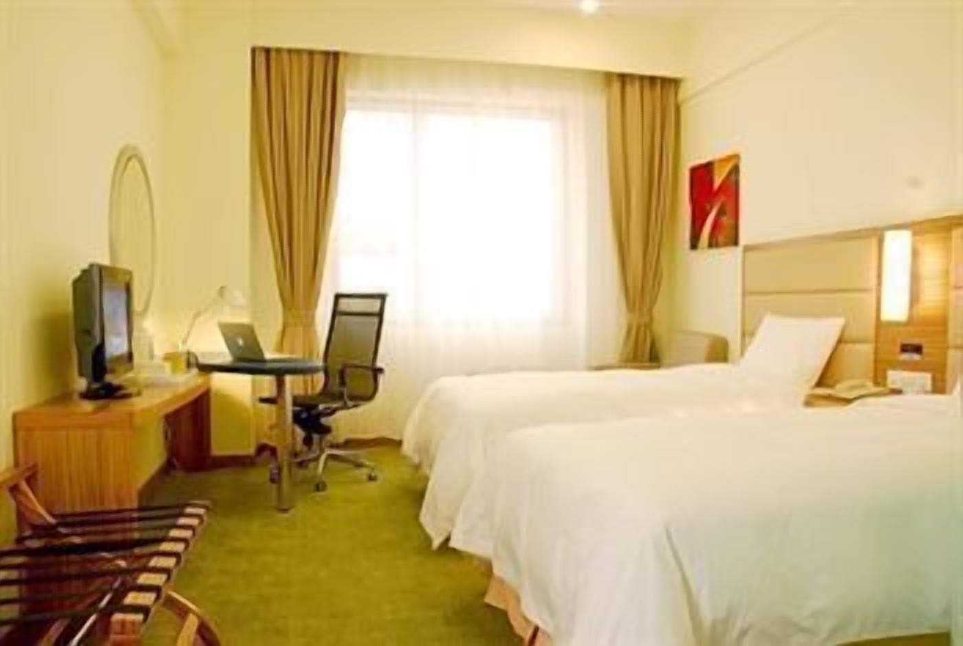 Et hotelværelse med to senge, et skrivebord med en computer, et fjernsyn og en stol.