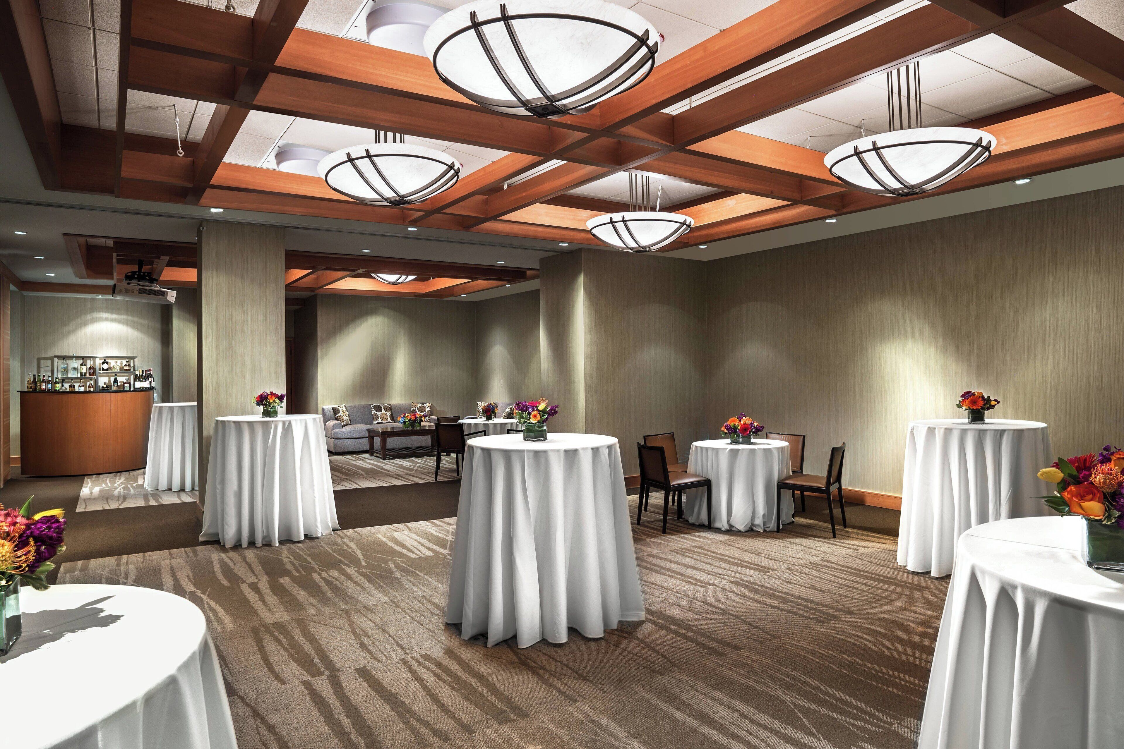 A hotel lobby with round tables covered in white tablecloths, a reception desk, and a bar area.