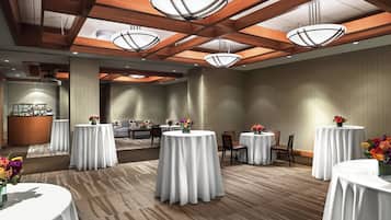 A hotel lobby with round tables covered in white tablecloths, a reception desk, and a bar area.