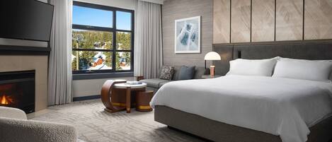 A modern hotel room with a large bed, a fireplace, a sofa, a small table, and a TV.