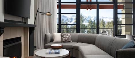 A modern living room with a large sectional sofa, a fireplace, a flat-screen TV, and a view of mountains through large windows.