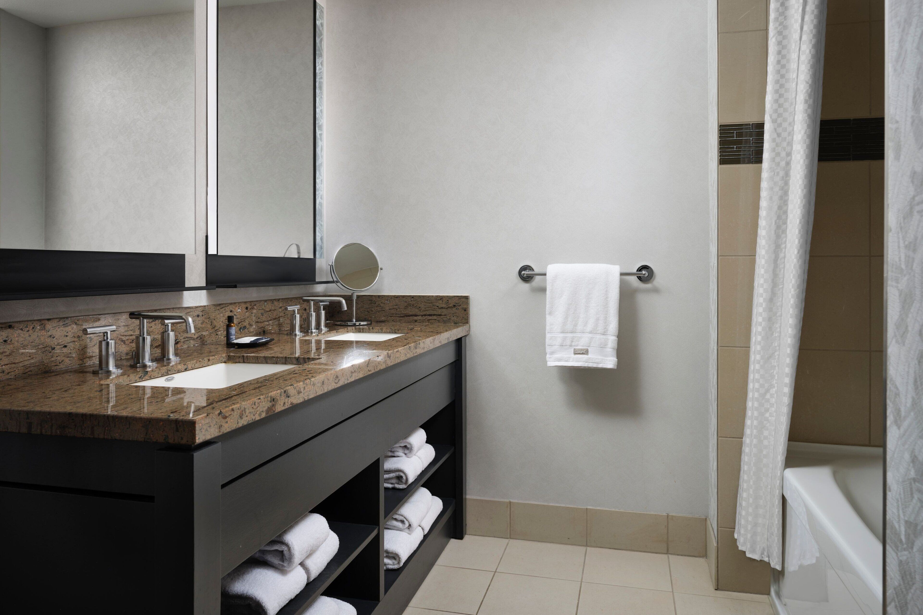 Un baño moderno con encimera de granito, dos lavamanos, un espejo y un perchero para toallas.