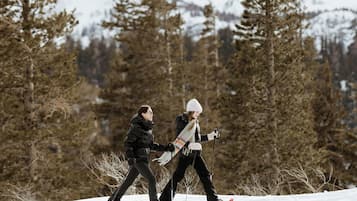 Two people cross-country skiing on a snowy slope with trees in the background.