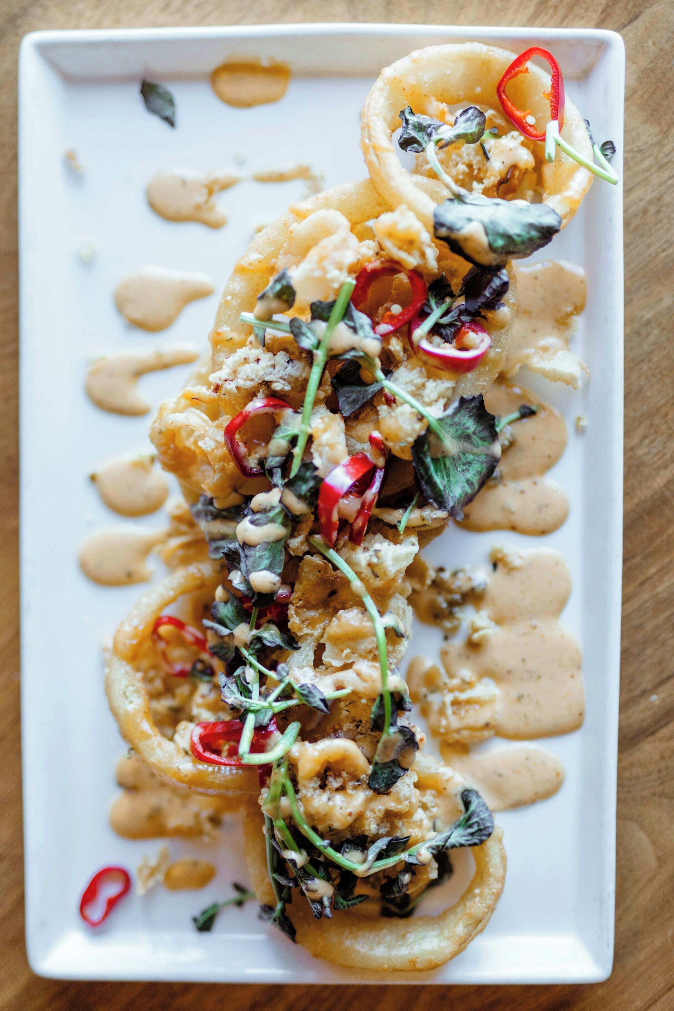 A rectangular plate with a food dish, garnished with red chili slices and greens, and a creamy sauce.