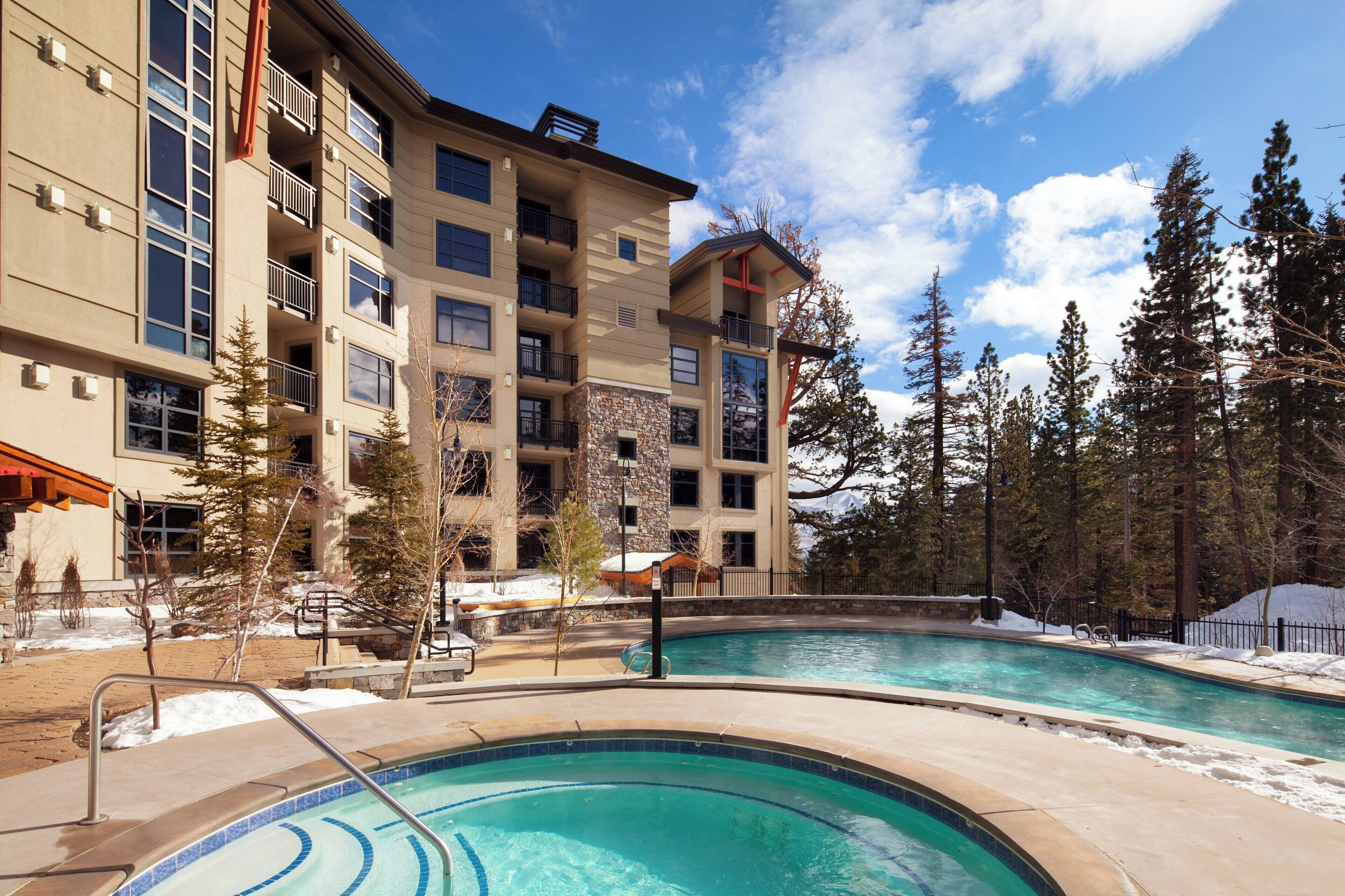 A hotel with a pool, stone facade, and multiple balconies.