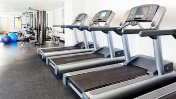 File di tapis roulant in palestra, con attrezzature per esercizi e uno specchio sullo sfondo.