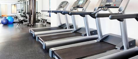 Eine Reihe von Laufbändern in einem Fitnessstudio mit Trainingsgeräten und einem Spiegel im Hintergrund.