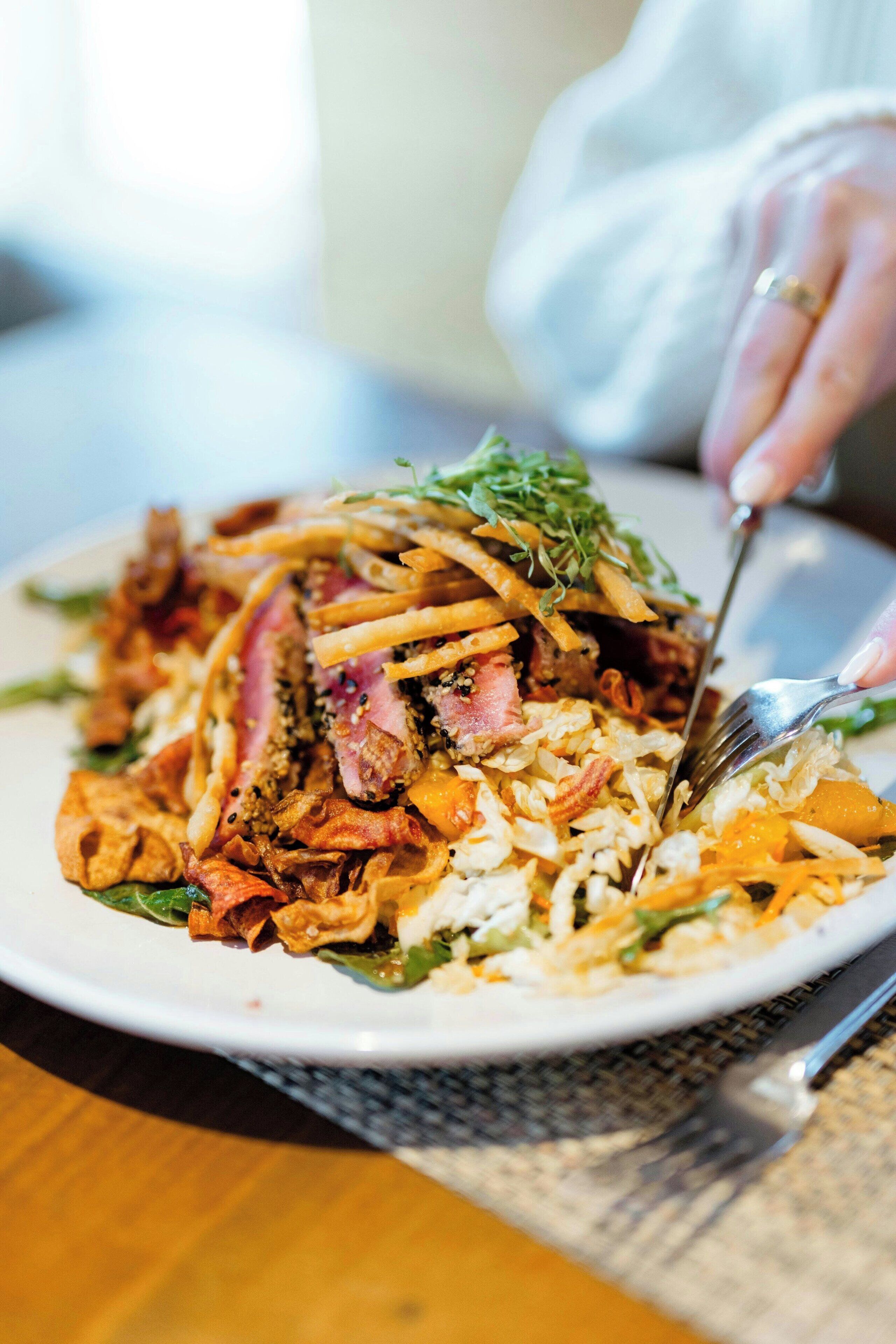 Una persona tiene una forchetta sopra un piatto di cibo, con carne e verdure.