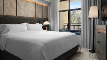 Una cama bien hecha con sábanas blancas, un cabecero de madera y una mesita de noche con una lámpara.