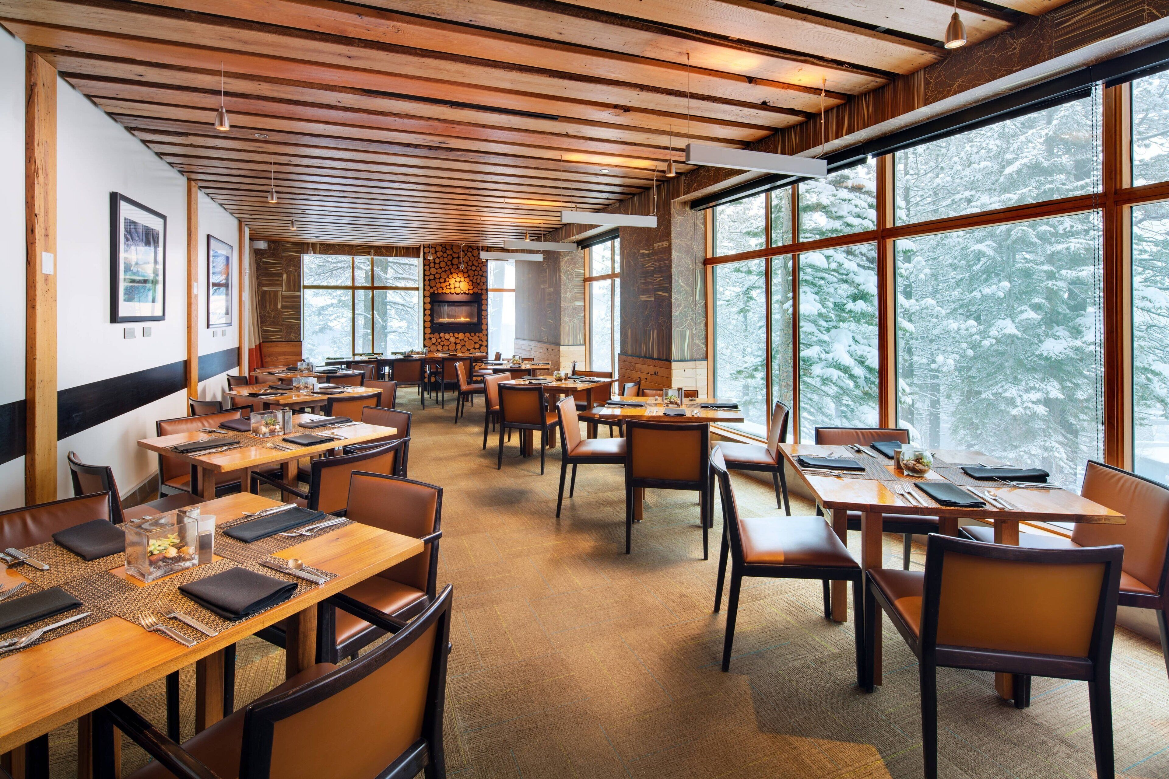 Un'ampia sala da pranzo con diversi tavoli e sedie, grandi finestre che offrono vista innevata e un soffitto in legno.