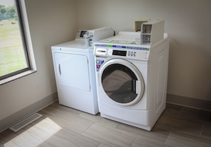 A compact, white front-loading washing machine with a digital display and control panel, situated in a laundry room with a window and a vent. - Holiday Inn Express Hotel & Suites Athens by IHG (Athens)