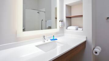 A modern bathroom with a large mirror, white sink, and wooden vanity.