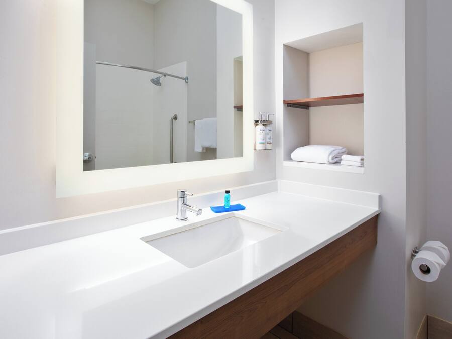 Une salle de bain moderne avec un grand miroir, un lavabo blanc et un meuble-lavabo en bois.