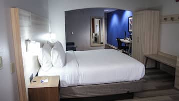 A hotel room with a large bed, a desk with a lamp, a wardrobe, and a bathroom visible through an archway.