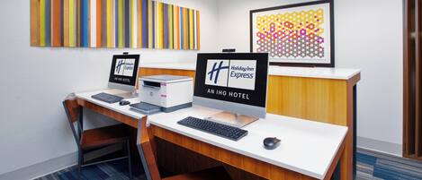 Un mostrador de recepción de hotel con dos monitores de ordenador, un teclado y un ratón. Hay dos carteles enmarcados en la pared, uno para el hotel y otro para Holiday Inn Express. La habitación tiene una alfombra azul y un escritorio de madera.