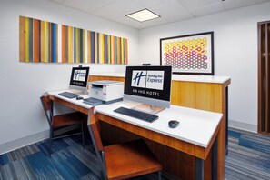 Een hotel receptiebalie met twee computermonitoren, een toetsenbord en een muis. Twee lijstjes aan de muur, één met de hotelnaam en één met Holiday Inn Express. De kamer heeft een blauw tapijt en een houten bureau.