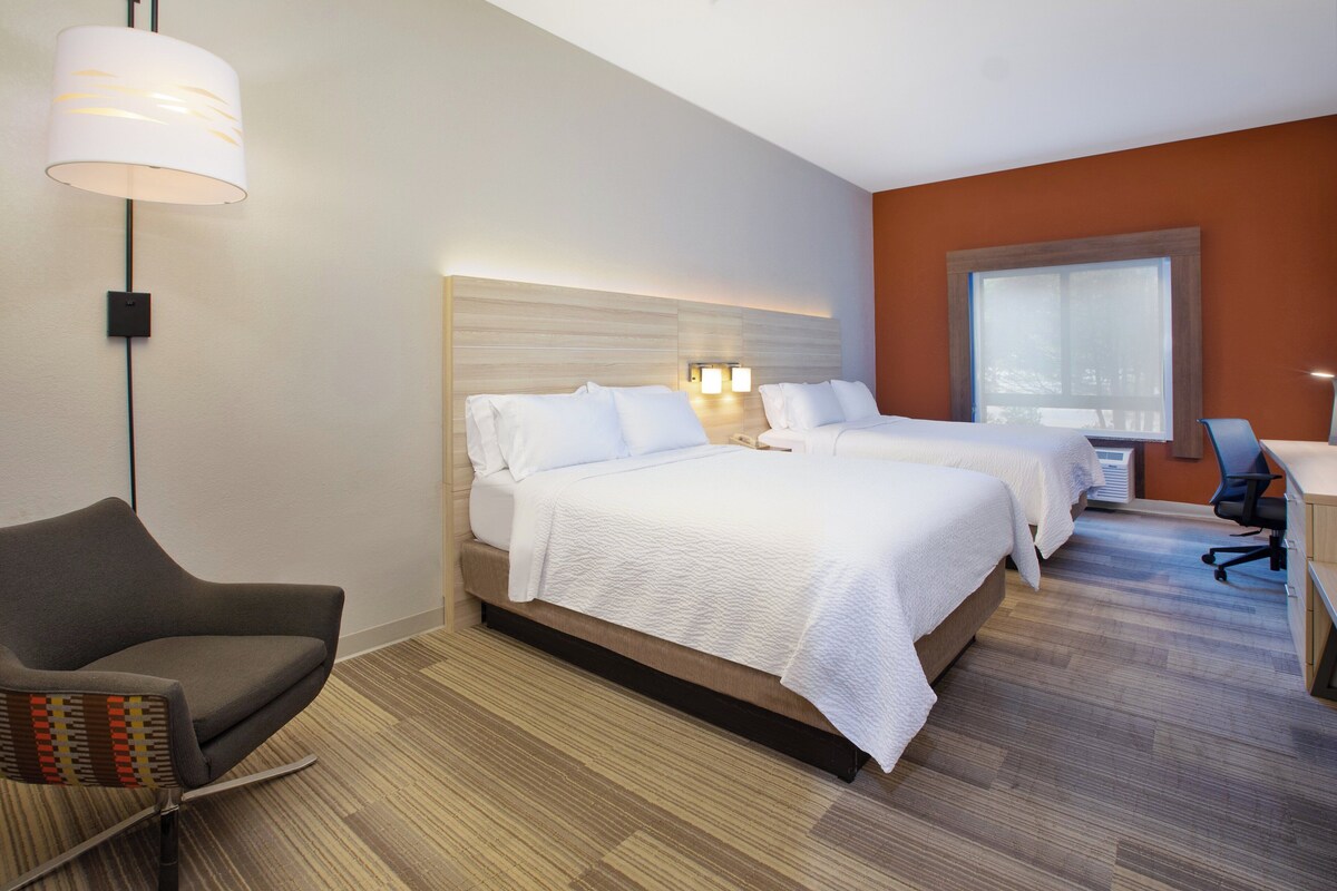 Een hotelkamer met twee bedden, een bureau, een stoel en een groot raam.