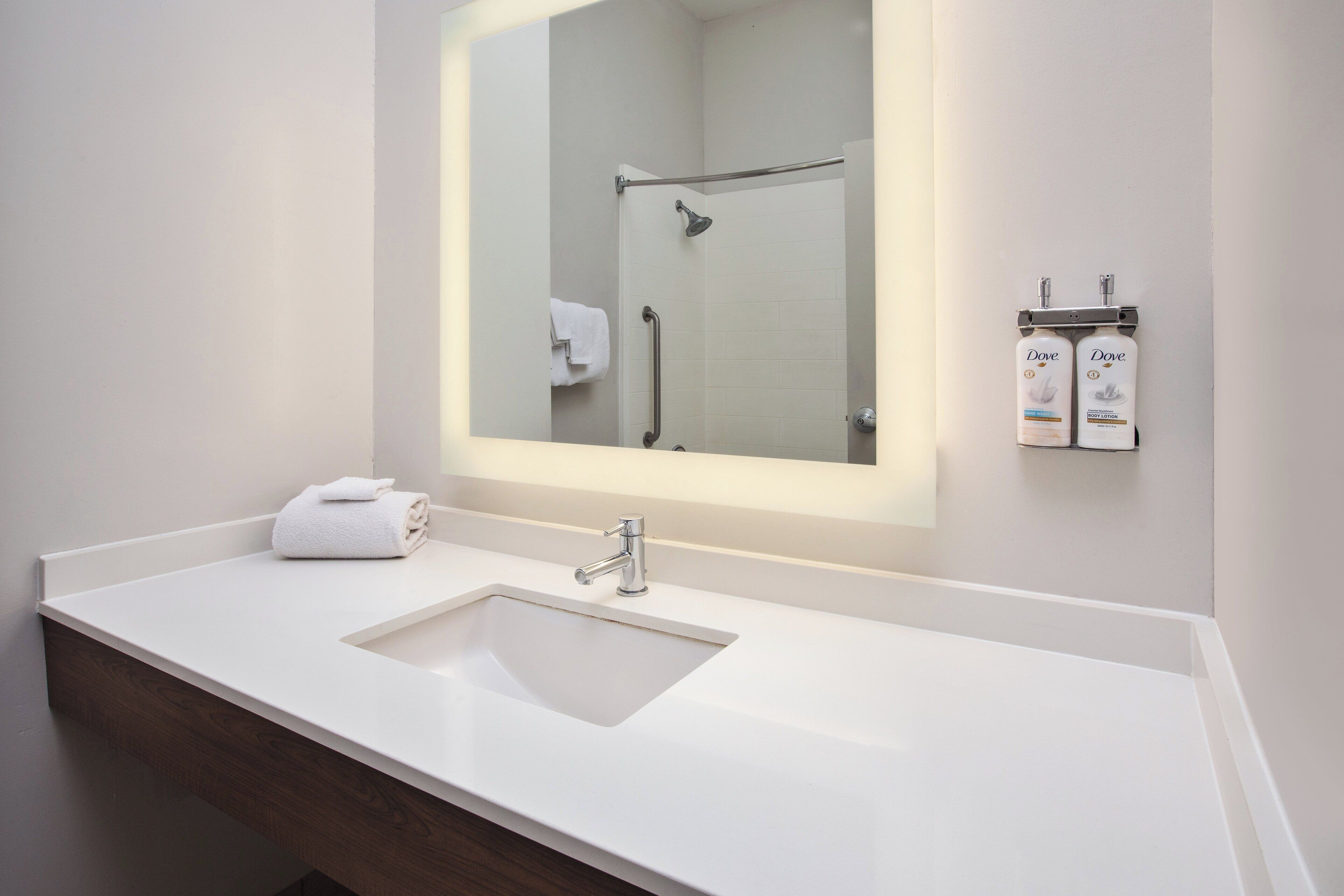 A modern bathroom with a white sink, a large mirror, and a shower area.