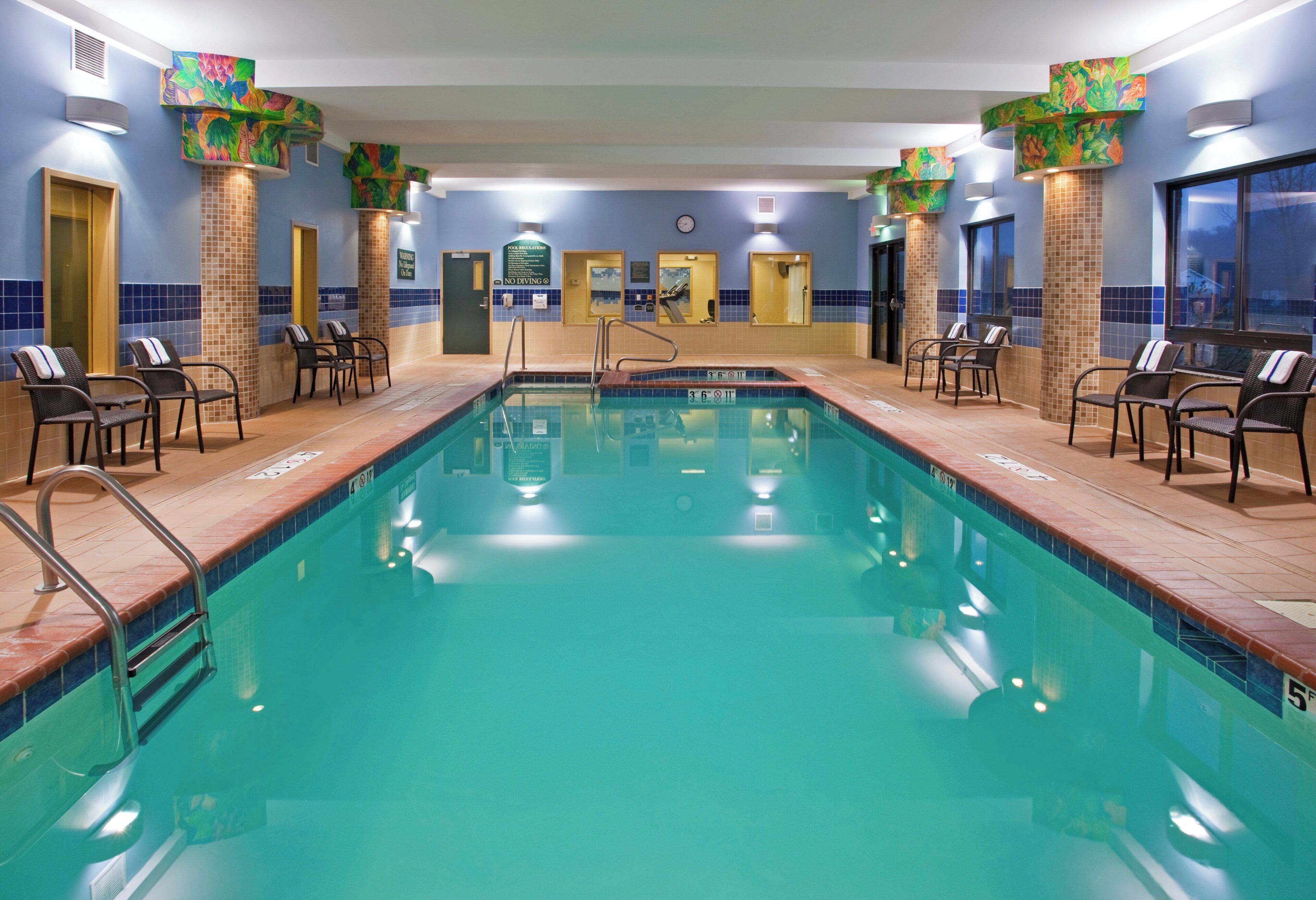 A swimming pool with multiple lanes, surrounded by lounge chairs and a clock on the wall.