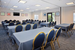 Een congreszaal met meerdere tafels en stoelen, een flatscreen televisie aan de muur en lijstwerken aan de wanden.