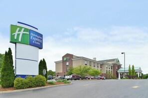 Un Holiday Inn Express & Suites con un letrero grande, edificio de ladrillo, estacionamiento y jardines.