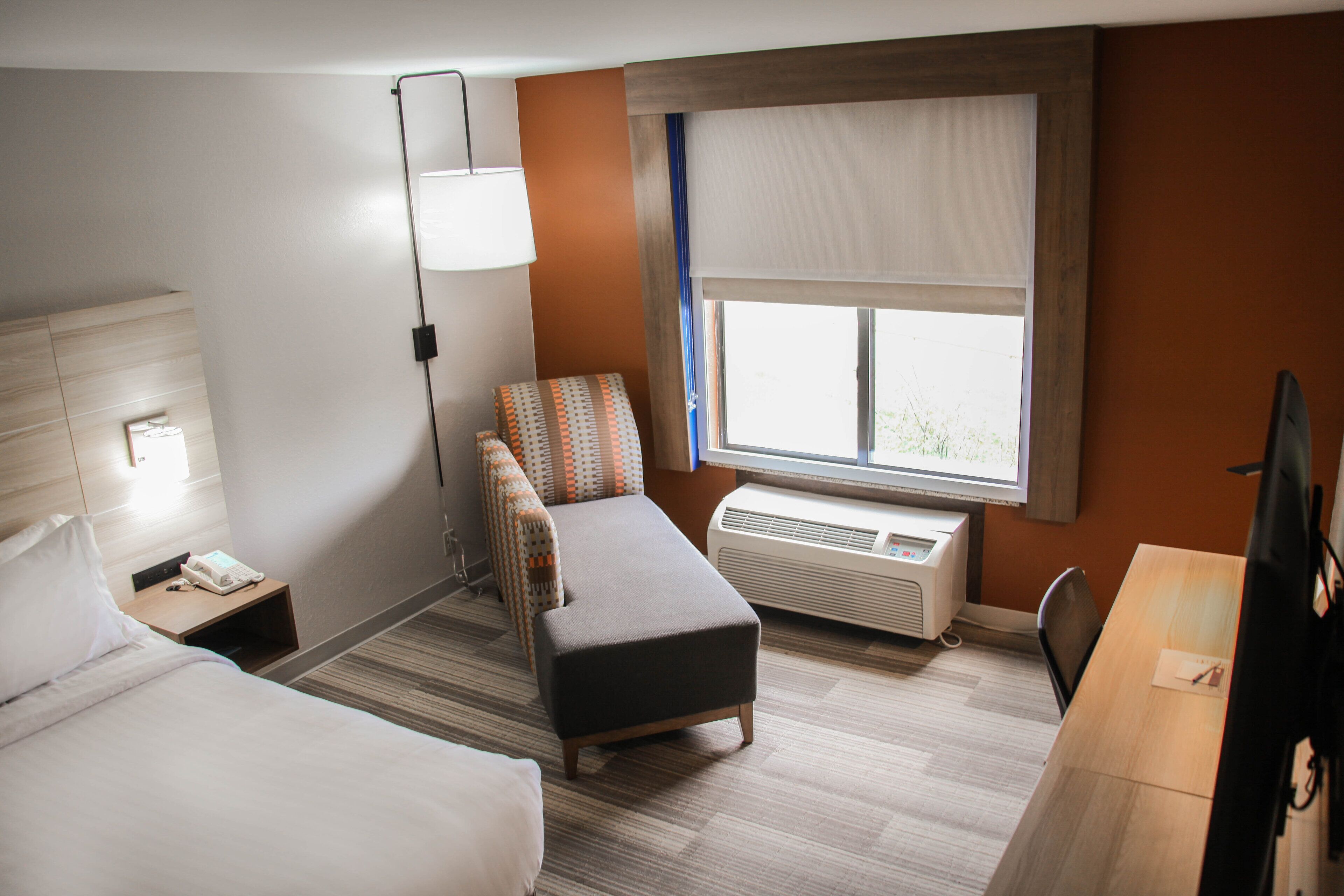 A hotel room with two beds, a desk, a chair, a lamp, an air conditioner, and a window with a view.