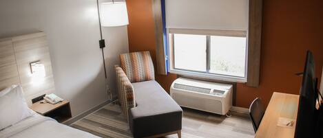 A hotel room with two beds, a desk, a chair, a lamp, an air conditioner, and a window with a view.