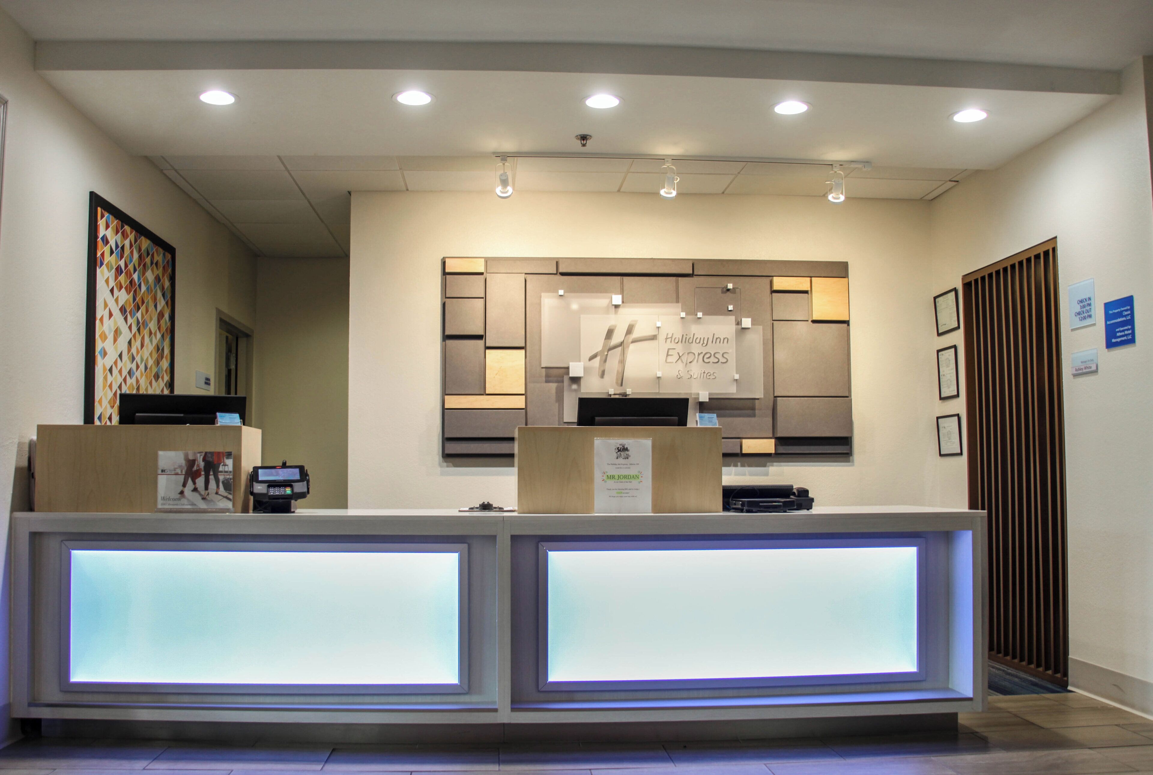 A reception desk with a digital display, a framed welcome sign, and a wall-mounted information board.