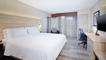A hotel room with a large bed, a desk with a computer, a chair, and a television.