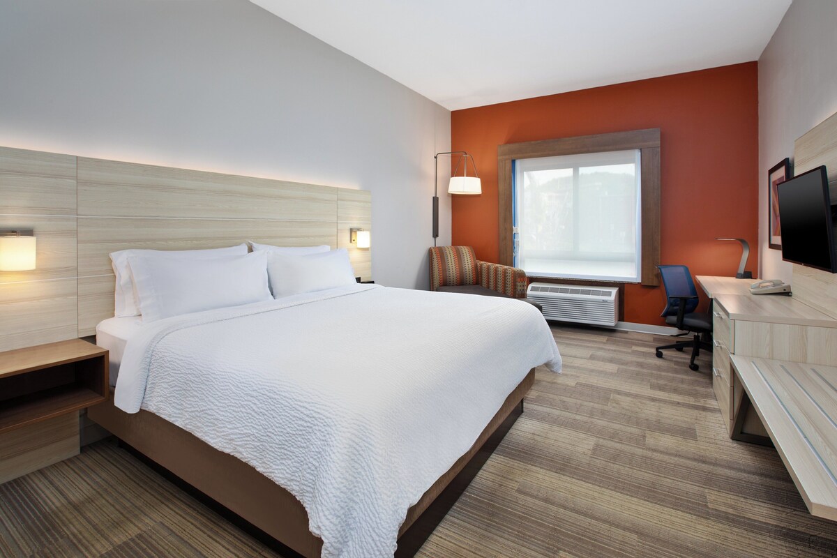 Een hotelkamer met een groot bed, een bureau, een stoel, een televisie en een raam met jaloezieën.