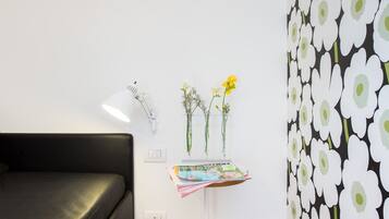 Una stanza moderna con un divano nero, una lampada bianca, un tavolino con dei fiori e una parete decorata con un motivo floreale.