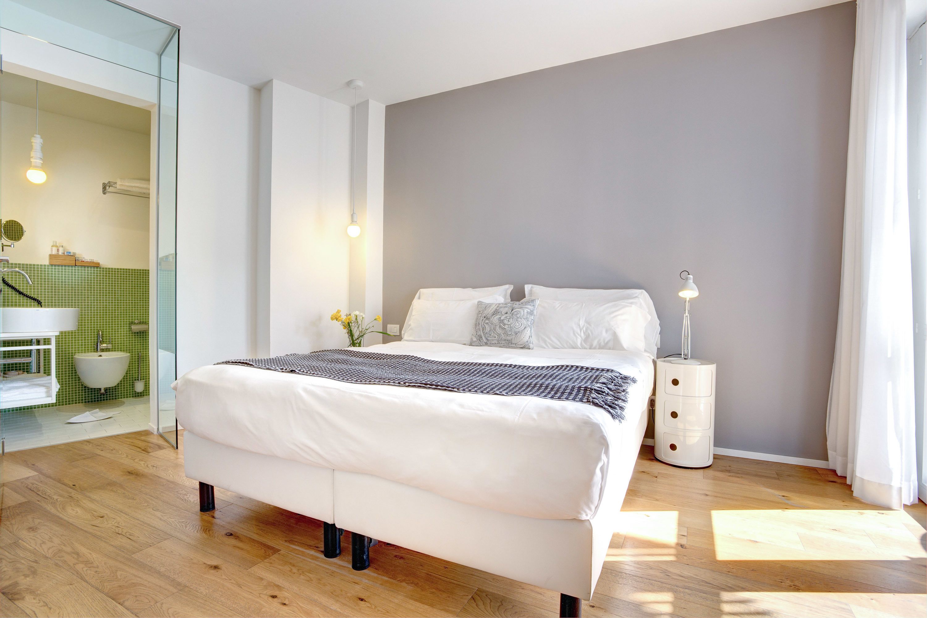A modern bedroom with a large bed, a bedside table with a lamp, and a glass-enclosed bathroom.
