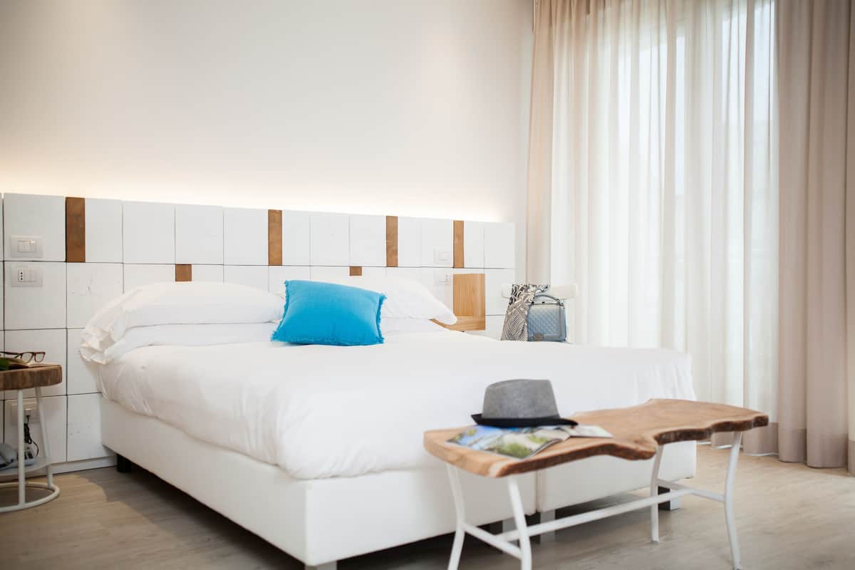 Una habitación de hotel moderna con una cama bien hecha, una mesita de madera y una lámpara de noche.