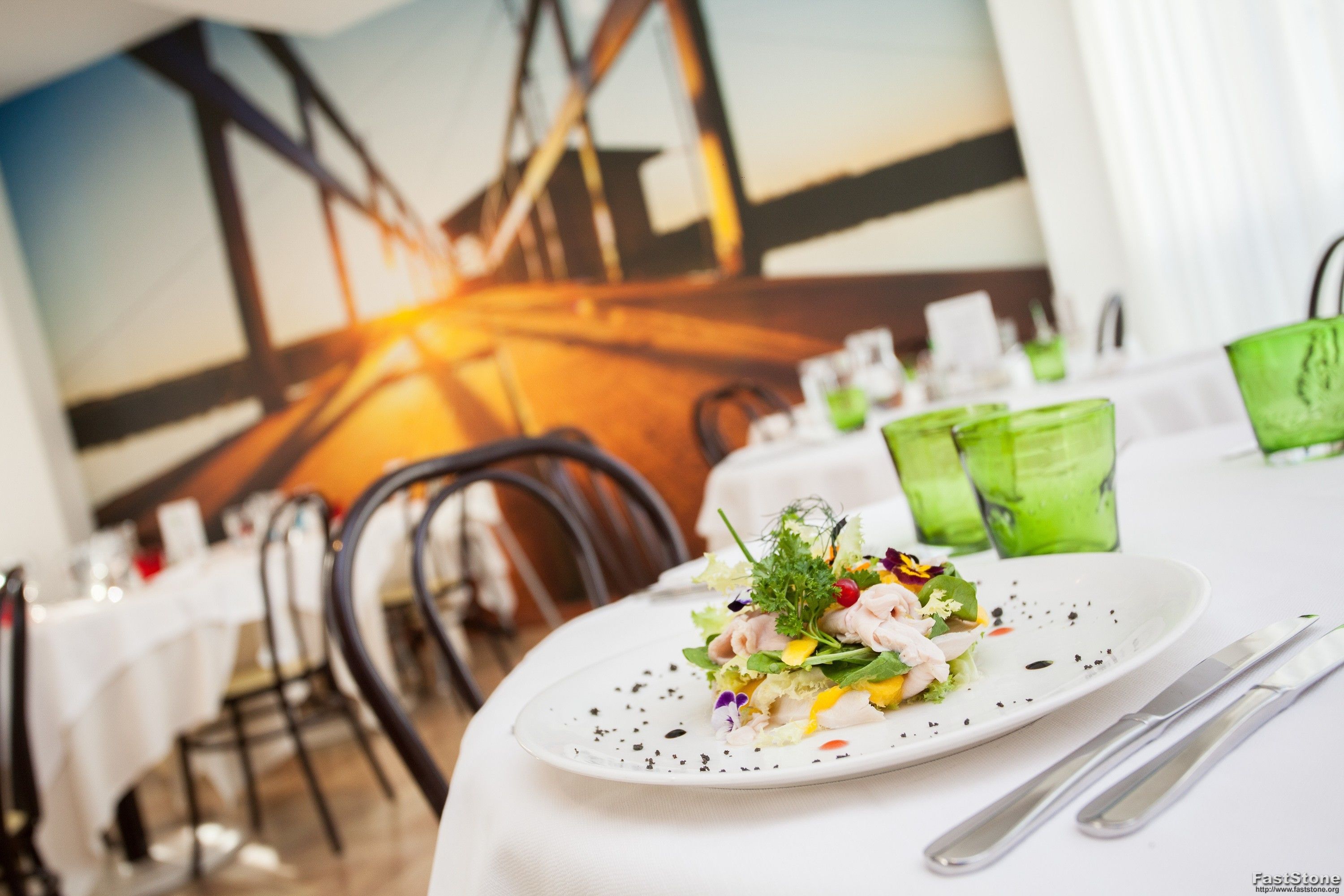 A restaurant setting with a white tablecloth, a plate of food, and a green glass.
